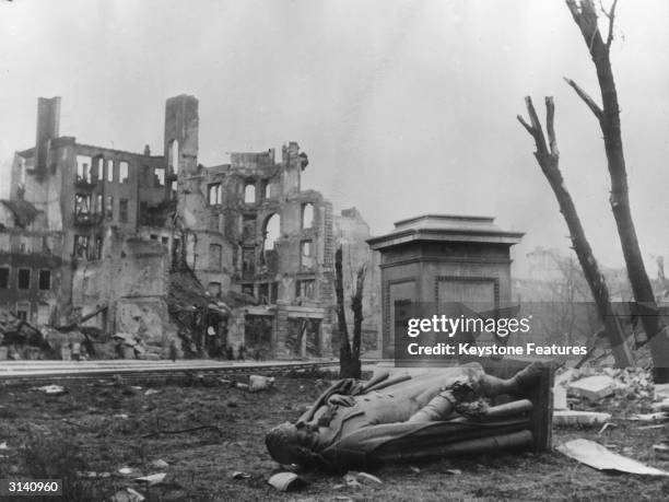 Statue of the German poet Johann Schiller lies on the ground beside its pedestal in war torn Munich just after the end of WW II..