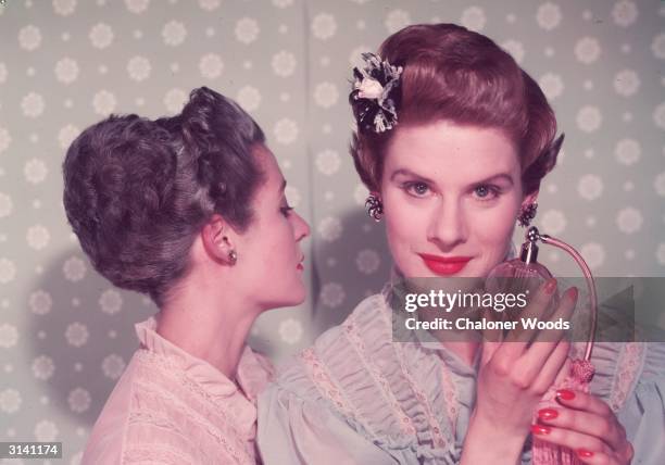 Woman with bright red nail varnish sprays herself with perfume using an atomiser.