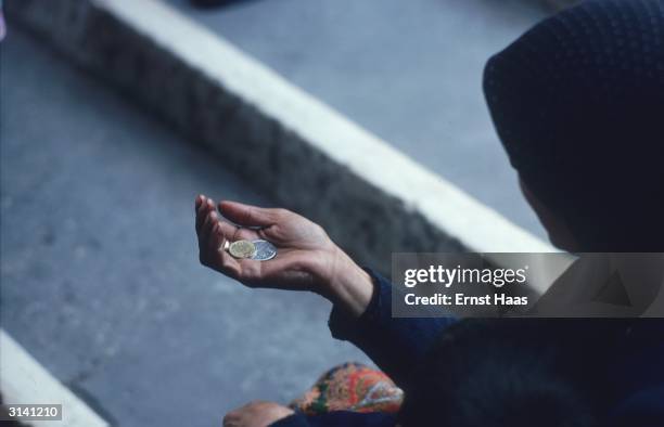 Beggar woman holds out her hand for money, two coins already in her palm.
