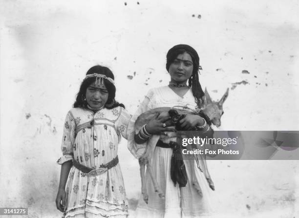 Two girls in the old town of Biskra, Algeria. Both have henna markings on their faces and one carries a young fawn.