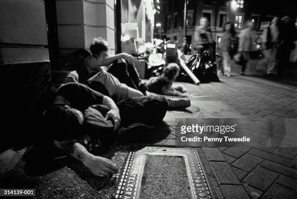 homeless people with dogs huddled together on pavement, night (b&w) - homeless fotografías e imágenes de stock