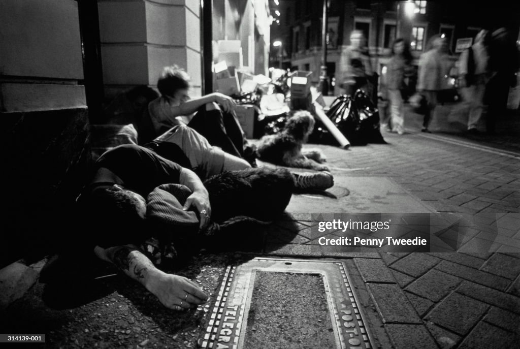 Homeless people with dogs huddled together on pavement, night (b&w)