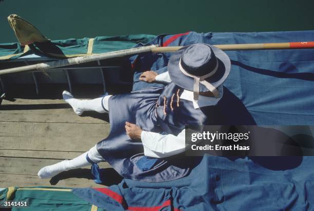 Gondolier in traditional livery takes a nap in his vessel.
