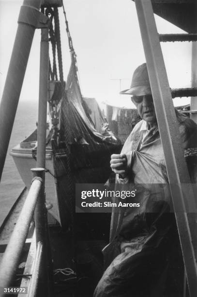 Director John Ford takes shelter during a tropical storm which interrupted the filming of 'Mister Roberts', a Warner production.