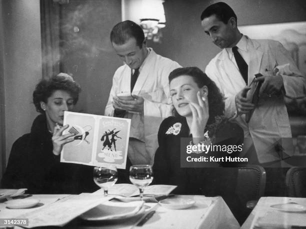Couple of waiters taking the order of two women from the menu at the Eve nightclub in the Place Pigalle, Paris. Original Publication: Picture Post -...