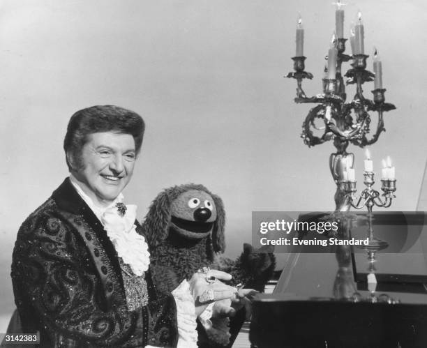 Flamboyant American pianist, singer and entertainer Liberace playing the piano with a little help from the Muppets piano dog, Rowlf.