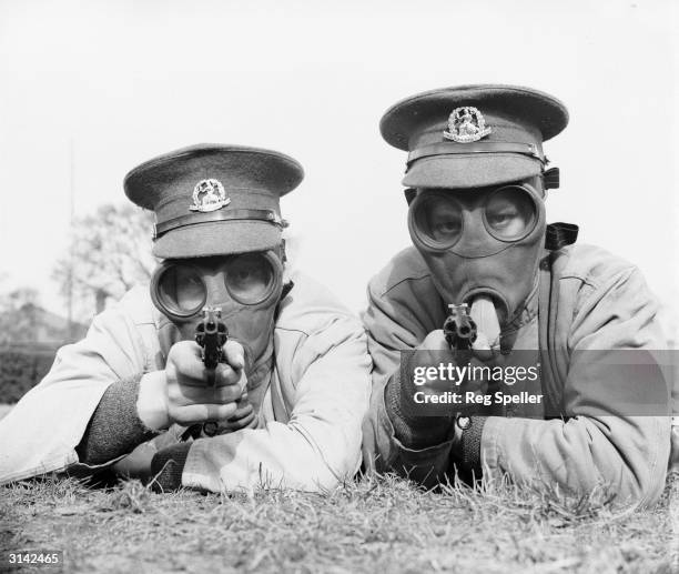 Soldiers of the Royal Norfolk Regiment at Aldershot, Hampshire getting used to revolver shooting while wearing a gas mask.