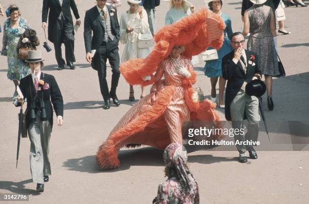 At Ascot races Mrs Gertrude Shilling in an apricot coloured, feather trimmed out fit, which is completed by an enormous, matching, cartwheel hat.