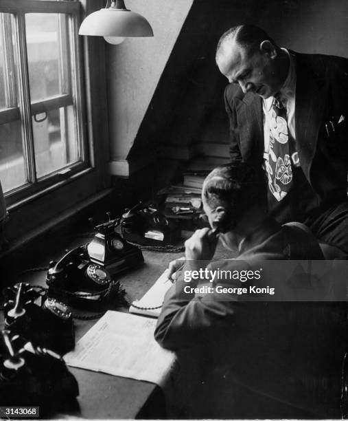 Bookmaker and boxing promoter Jack Solomons watching his manager, B Waller, take a bet by telephone.