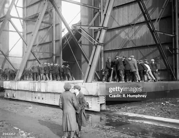 Crowd of men struggle with the door of the aerodrome hangar which houses the British airship R33.