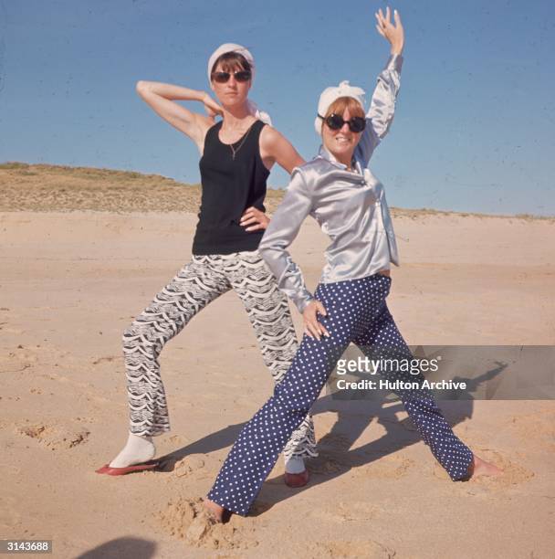 To r. TV presenter Cathy McGowan and on right, pop star and TV show hostess Cilla Black posing on the beach while on holiday in Portugal.