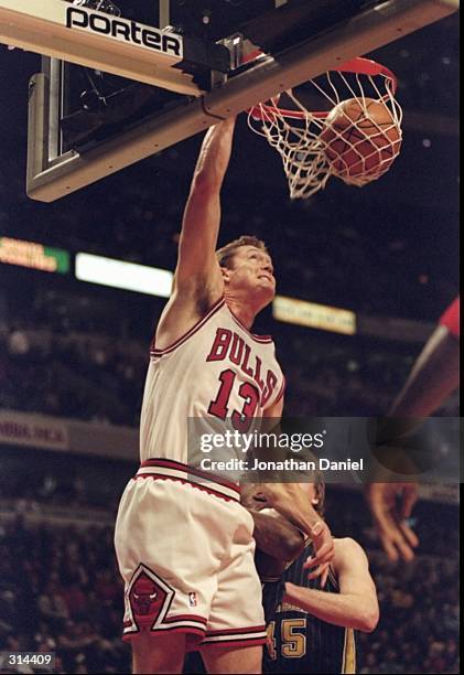 Center Luc Longley of the Chicago Bulls sinks the ball as center Rik Smits of the Indiana Pacers looks on during a game at the United Center in...