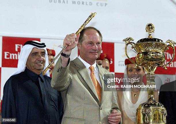 Trainer Richard Mandella raises the Dubai World Cup trophy he received from the ruler of Dubai Maktoum bin Rashed al-Maktoum after US jockey Alex...