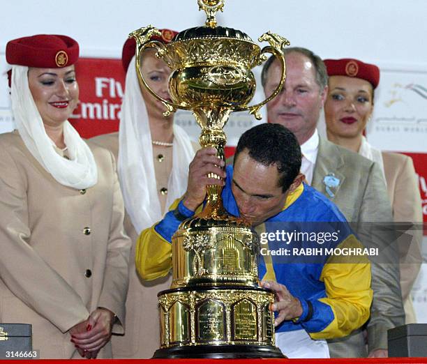 Jockey Alex Solis kisses the Dubai World Cup trophy as trainer Richard Mandella looks on 27 March 2004. Solis on Pleasantly Perfect won ahead of...