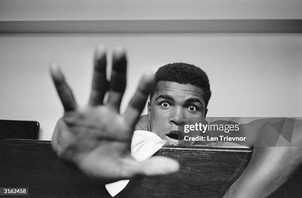 American Heavyweight boxer Cassius Clay lying on his hotel bed in London. He holds up five fingers in a prediction of how many rounds it will take...