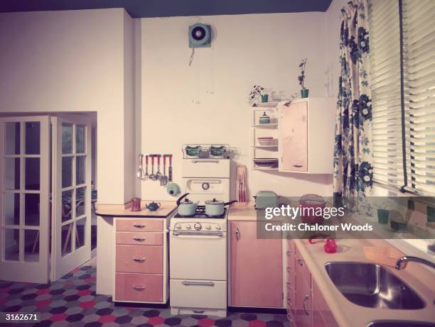 Interior of a fifties fitted kitchen with a linoleum tiled floor and venetian blinds.