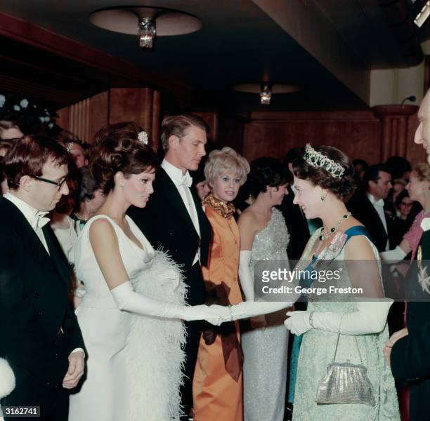 American actress Raquel Welch shaking hands with Queen Elizabeth II of Great Britain at a Royal Film performance. Next in line is the American...