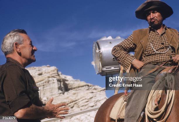 Film director William Wyler talking to a cast member on the set of his western 'The Big Country'.