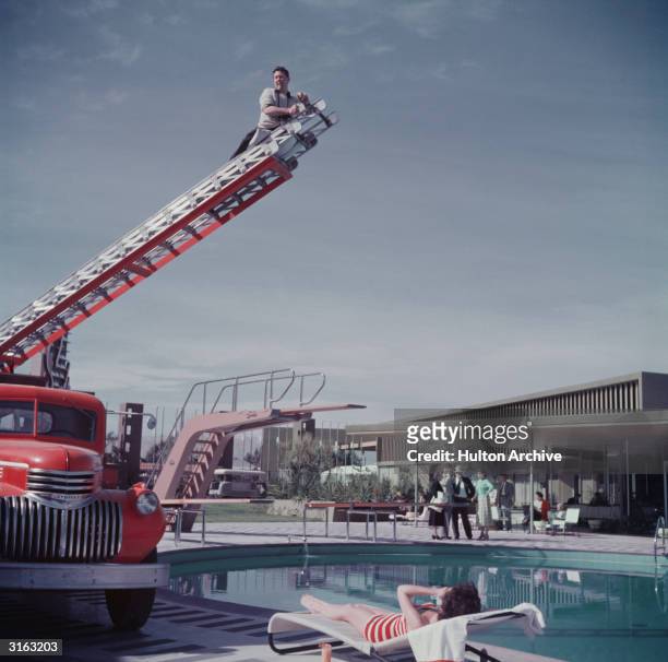 Photographer Slim Aarons photographing film starlet Mara Lane from the top of an extending ladder by the swimming pool at Sands Hotel, Las Vegas.