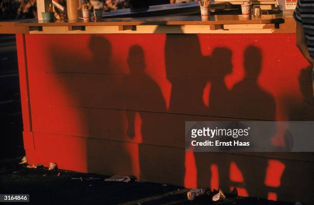 Shadows of customers on the red sides of a drinks stall.