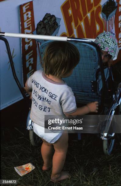 Toddler pushes a little girl in a pushchair.