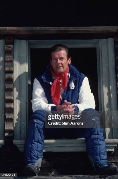 Actor Roger Moore wearing salopettes and sitting in a window in Gstaad, Switzerland.