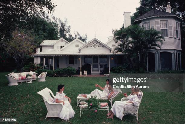 Three women relaxing in front of a white clapperboard house in Palm Beach, Florida. Left to right, Hilda Juliette Arias de Rey Millet, Maria Victoria...