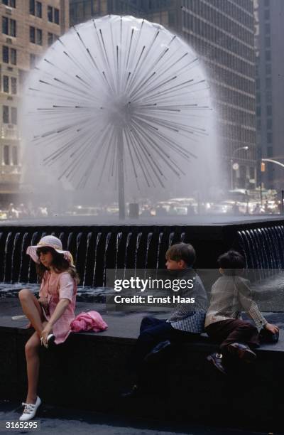 In New York children sit by a fountain that looks like a large dandelion 'clock'.