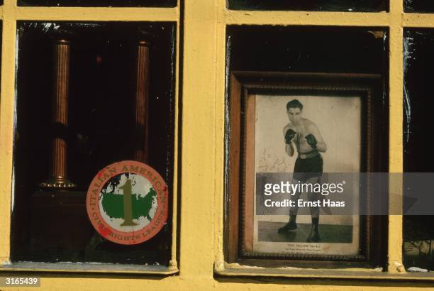 Yellow painted window of the 'Italian American Civil Rights League' displaying their logo on one side and on the other a photograph of boxer Tony...