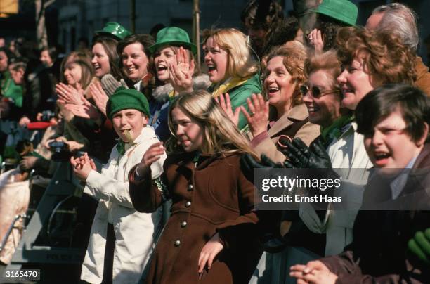 Part of the crowd watching Macy's Thanksgiving Day Parade some of whom are wearing green hats.