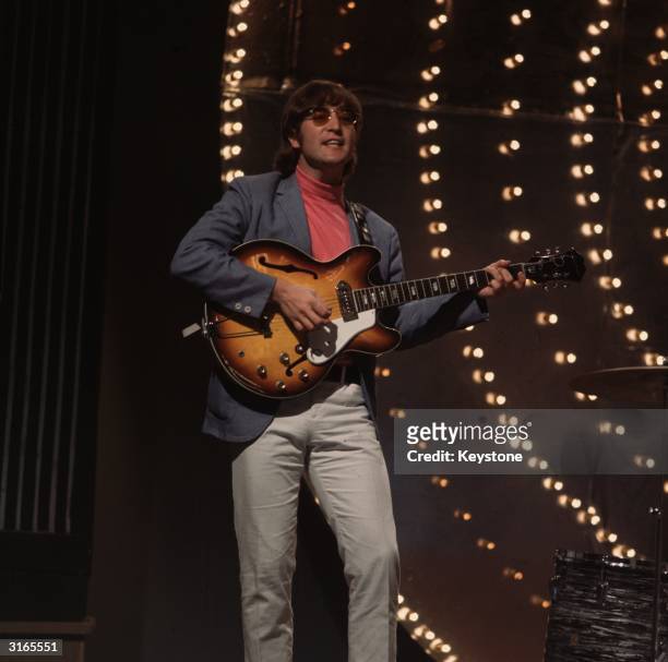 Beatles singer, songwriter and guitarist John Lennon performing against a lit backdrop.
