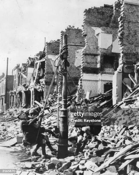 Young boys swinging from a lamp post in the midst of rubble left by a bombing raid on London during the Blitz.