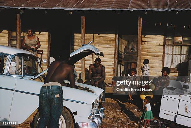 Man checks his car engine in front of a row of slum housesand their inhabitants in a shanty town in New Orleans, Louisiana.