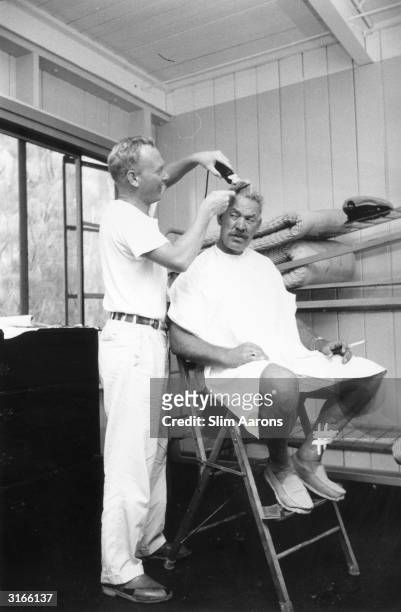Actor Harry Carey Jnr shaves the head of Ward Bond during the filming of John Ford's 'Mister Roberts' on location in Hawaii. Bond plays Chief Petty...