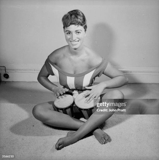 Actress Jackie Collins playing the bongos in her London flat.