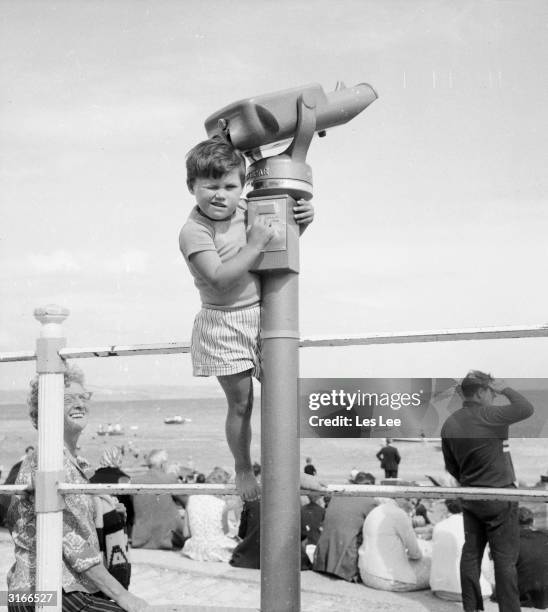 Little boy pulling a face while clambering up a telescope on the front at Weymouth.