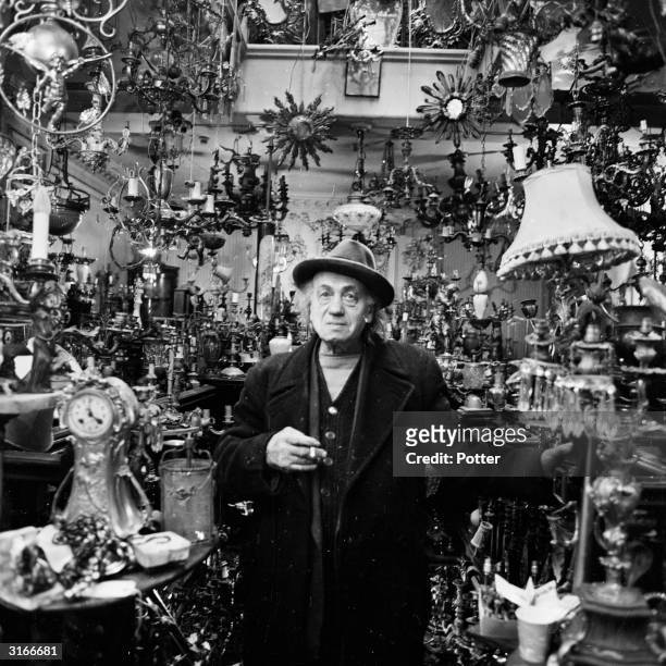 Mr Jacob Mendelson a junk dealer standing in his shop surrounded by clocks, lampstands and various oddities.