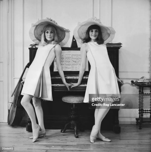 Film actress Catherine Deneuve and her older sister Francoise Dorleac posing against a piano on location for the film 'Les Demoiselles de Rochefort'...