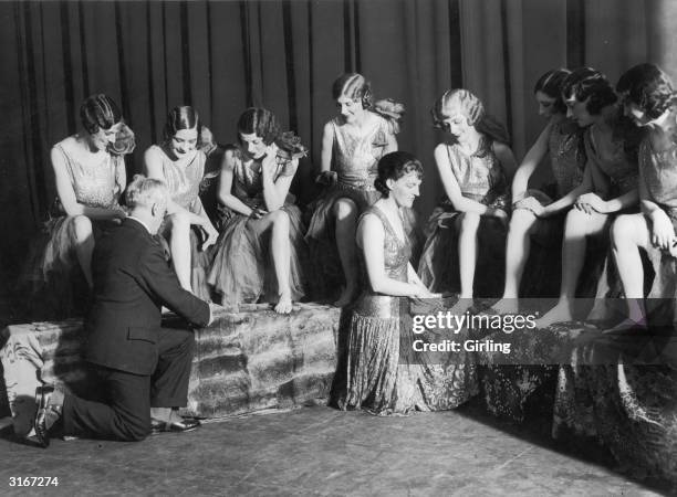 Mr Coffey and Gracie Fields kneel down to judge the winner of a Beautiful Feet Contest. All the contestants are chorus girls from 'The Show's The...