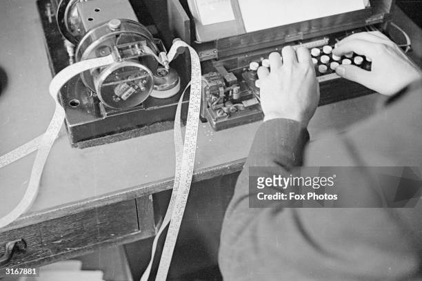 Man using a ticker tape machine attached to a typewriter keyboard at a Press Association and Reuters office.