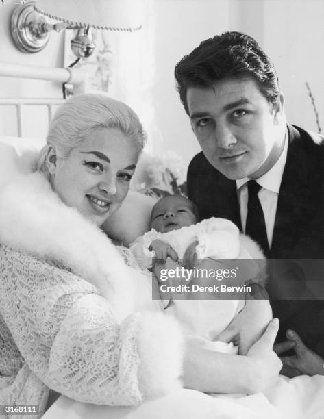 In swansdown trimmed bedjacket film star Diana Dors cuddles her first baby, Mark Richard. With them in the London Clinic where the baby was born is...
