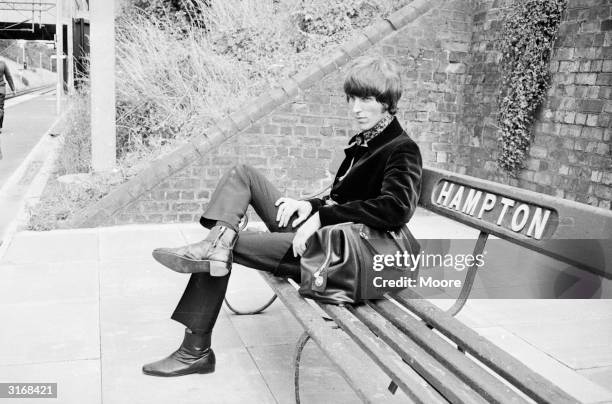 Radio Caroline disc jockey Johnnie Walker sitting on a Hampton bench with a leather bag.