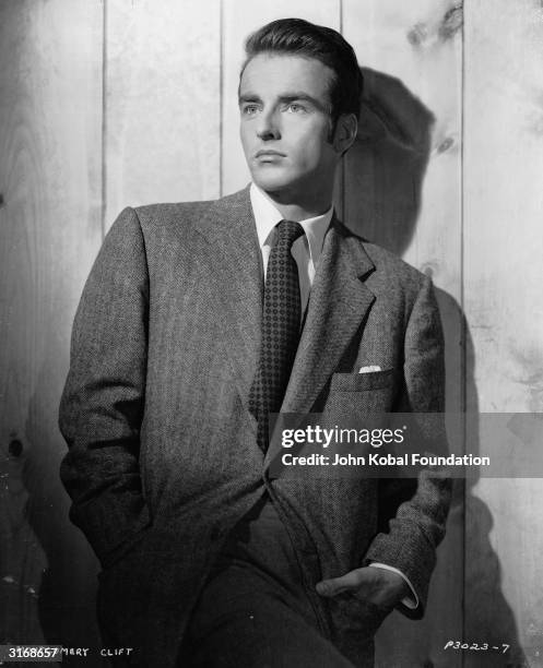 American actor Montgomery Clift lounges against a fence in a smart suit.