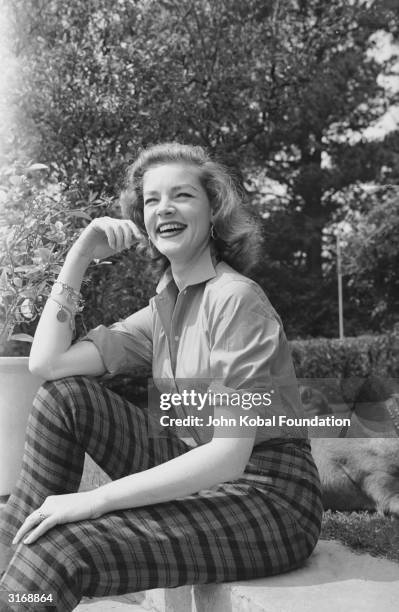 American screen star Lauren Bacall wearing checked trousers and a charm bracelet.