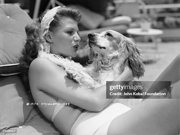 American film actress Rita Hayworth lavishes affection on her pet spaniel.