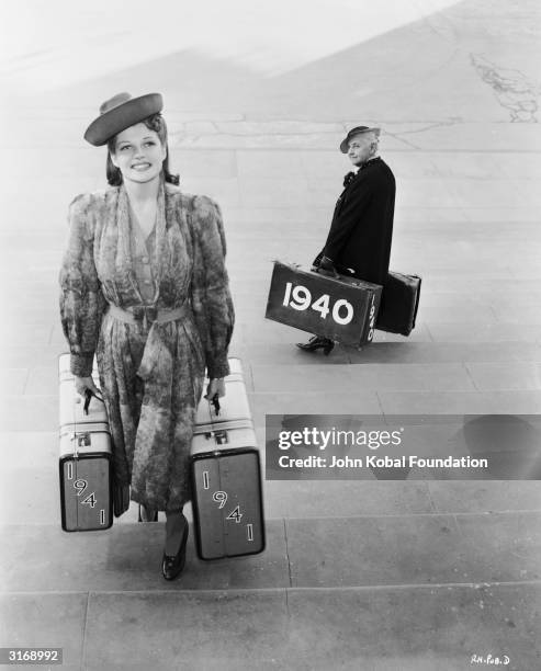 Young Rita Hayworth sees in the New Year with a pair of '1941' suitcases as she passes writer Quentin Crisp carrying a pair of '1940' suitcases on...