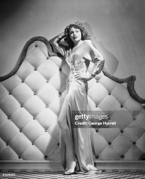 American actress Rita Hayworth wearing a floor-length gown with a slit up the front.