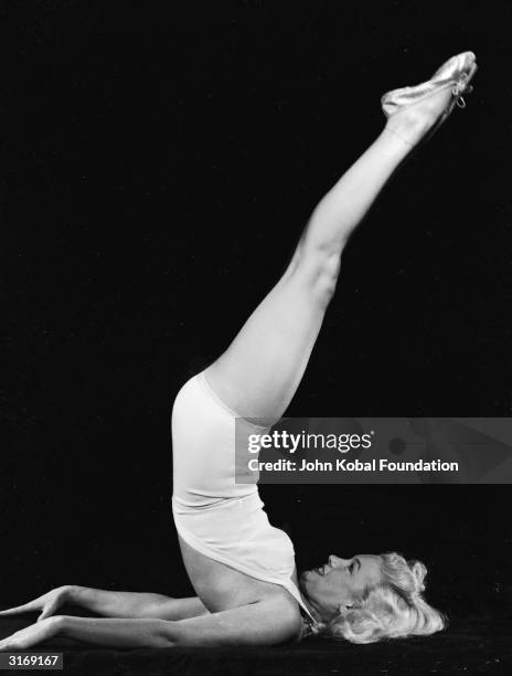 American film star Marilyn Monroe raises her legs in the air and assumes a yogic exercise position.