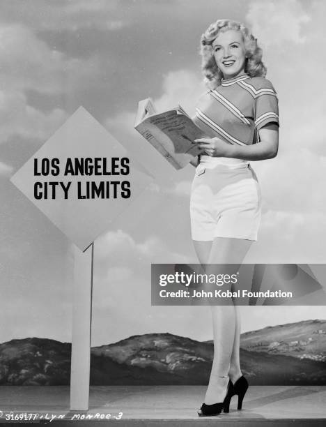 American film star Marilyn Monroe reading an LA telephone directory near the Los Angeles city limits.