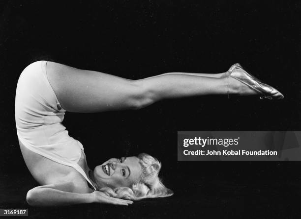 American film star Marilyn Monroe raises her legs in the air and assumes a yogic exercise position.